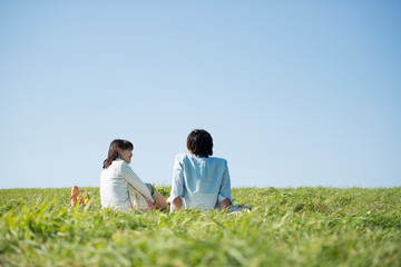 草原でピクニックをするカップルの後ろ姿