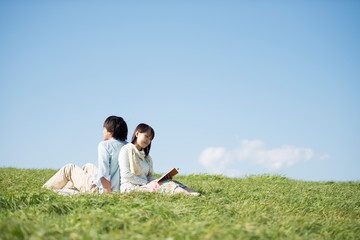 Fototapeta na wymiar 草原で音楽を聴く男性と読書をする女性