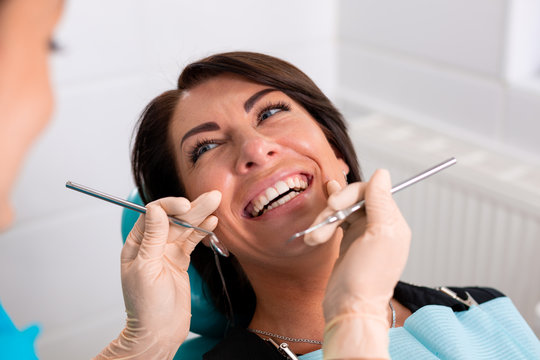 A dentist finishes a successful dental restoration, a doctor advises a happy patient, a beautiful long-haired woman looks at her clean, white, healthy teeth with great pleasure