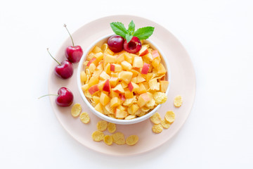 Healthy breakfast with cornflakes and pieces of fruit, cherries on a white background