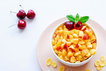 Healthy breakfast with cornflakes and pieces of fruit, cherries on a white background