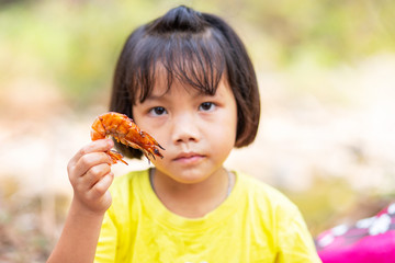 Naklejka premium Little Asian girl holding a piece of grilled shrimps