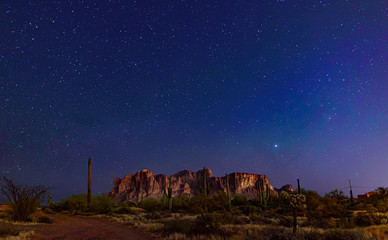 The desert wilderness east of Phoenix, Arizona photographed under clear starry desert skies that seem to glow with color. Desert plants and Saguaro cactus grow around the Superstition mountains 