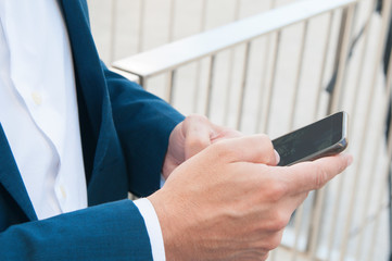 Hands of businessman using smartphone. Side view closeup of Caucasian man in formal jacket using cellphone, checking email, using app or texting message. Digital device concept