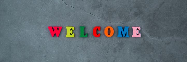The multicolored welcome word is made of wooden letters on a grey plastered wall background.