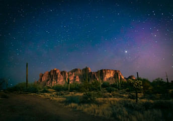 The desert wilderness east of Phoenix, Arizona photographed under clear starry desert skies that seem to glow with color. Desert plants and Saguaro cactus grow around the Superstition mountains 