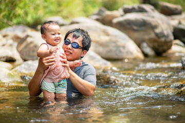 Fototapeta premium Asian man wearing goggles holding his baby girl in water