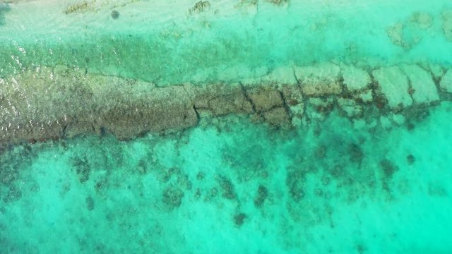 Flyover rocks inside turquoise water towards an island. In Jamaica. Dolly in