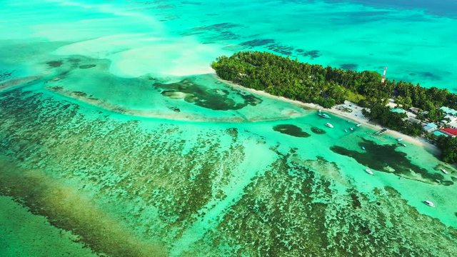 Aerial view of a flight next to a tropical island with a forest and village on it. The turquoise Sea of the Seychelles with reefs in it. Dolly in.