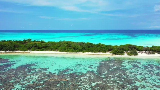 Aerial view, a thin tropical island with palm trees and paths. Turquoise shallow water with reefs in the foreground. The Philippines. Truck right