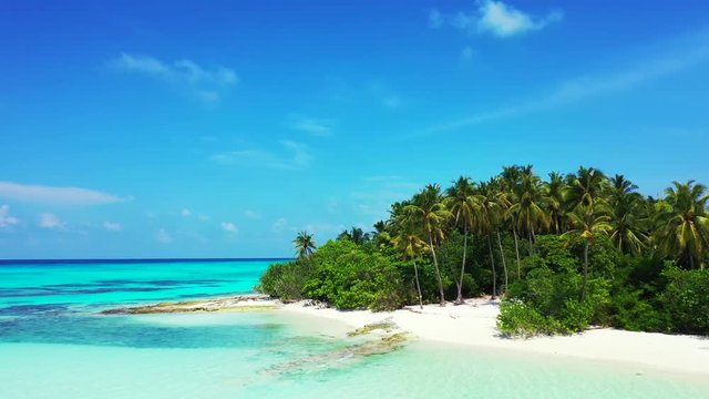 Aerial view, a tropical island with palm trees at a sandy beach. Turquoise water of the Philippines under a blue sky with clouds. Truck right, pan left