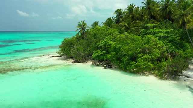 Aerial view of a tropical island with palm trees on it. turquoise water in front of it. the Bahamas under a blue sky. Truck slowly