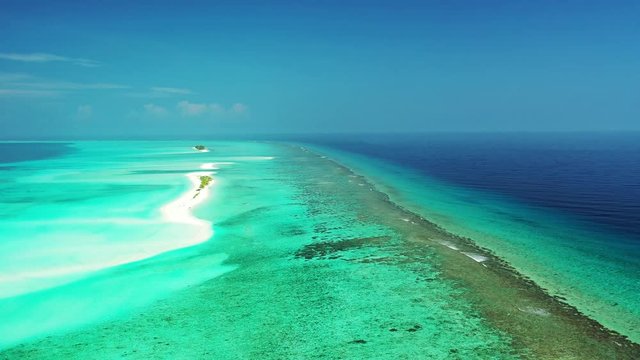 Flight over the turquoise green sea in Bali. Sandbanks in the water. A long reef to the right with the blue ocean next to it. Dolly in
