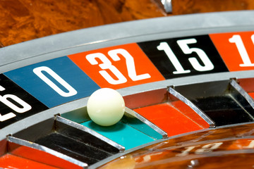 Roulette table in casino, with many games and slots, roulette wheel in the foreground.