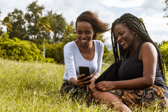 Two ladies sitting on the grass using a phone