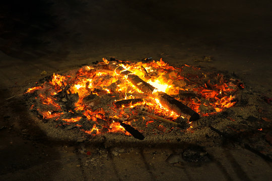A fire pit on a street after a celebration. The wood is still glowing and it is very hot.