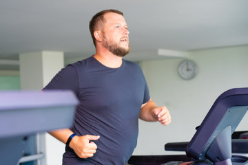 chubby man walking on running track, warming up on gym treadmill.