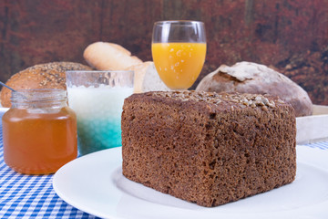 Orange juice, yogurt, jar of jam and a piece of multigrain bread served on a white plate