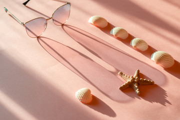 Seastar, seashells and pink sunglasses with metal frame cast a long shadow on the pink surface....