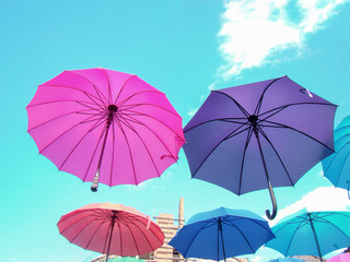 Colored umbrellas in the air. Colors - blue, green, red, crimson. Turquoise sky, cloud. Building.