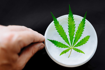 Macro close up of hand dosing cream of biological and ecological hemp plant herbal pharmaceutical CBD oil from jar