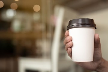 A woman holds a cup of coffee paper sitting in a coffee shop.
