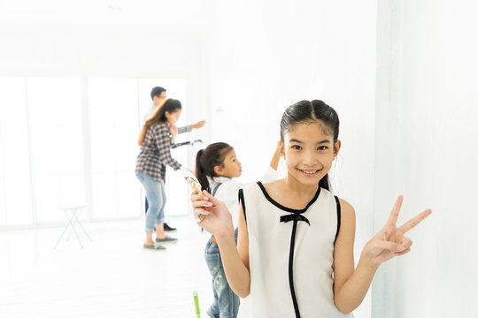 Happy Asian family renovating their new home and painting room wall. young girl smiling showing sign victory or success. interior restoration or refurbishment or repair, building and home concept