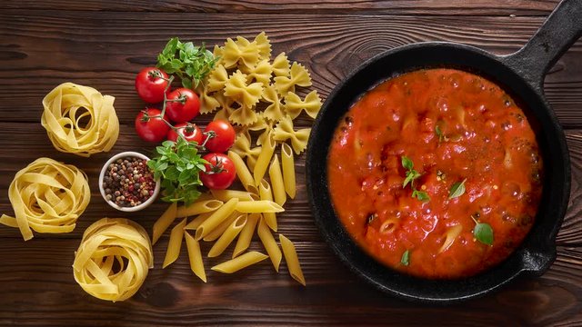 Cinemagraph loop. Cooking pasta penne with tomato sauce and basil on iron cast pan. Wooden table, top view