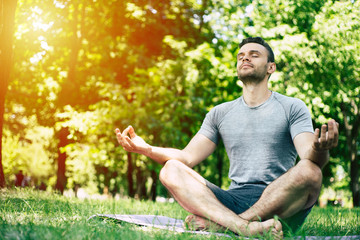 Naklejka na ściany i meble Male yoga relaxation. Sporty and slim handsome young man is doing yoga exercises in city park outdoors. Healthy lifestyle and strong soul and body
