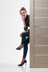 Beautiful woman peeking from behind the white door, isolated on white background with copy space