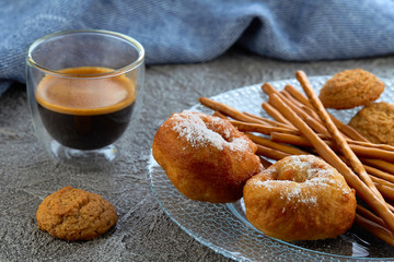 Two donuts on a plate, in the background of cup of espresso and blue kitchen towel.
