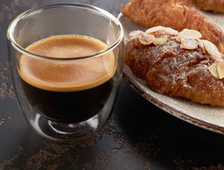 Cup of espresso and an almond croissant on a plate close-up. Delicious breakfast.