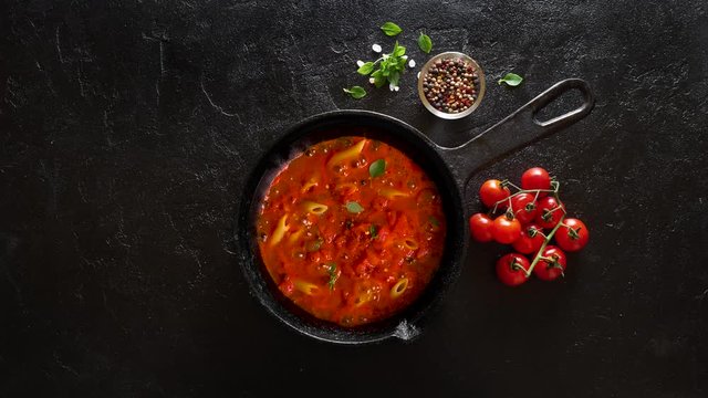 Cooking pasta penne with tomato sauce and basil on iron cast pan
