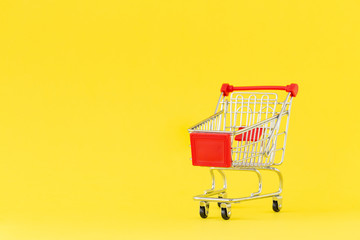 Shopping cart. Close-up of shopping trolley on yellow background. Concept of shopping. Copy space.   