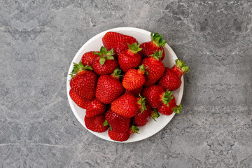 Red strawberry in a plate on grey background