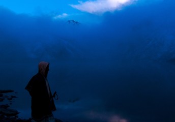 one mystery man wearing hood and stick in hand walking in early or wee hours of foggy winter morning on the mountains 