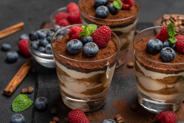 Classic tiramisu dessert with blueberries and raspberries in a glass on stone serving board on dark concrete background