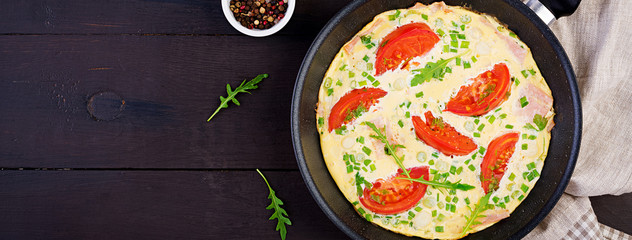 Omelette with tomatoes, ham and green onion on dark table.  Frittata - italian omelet. Banner. Top view