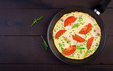 Omelette with tomatoes, ham and green onion on dark table.  Frittata - italian omelet. Top view