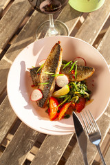 Fried mackerel fish with vegetable garnish: spinach in coconut milk, radish, onion and baked tomatoes, served on a sunny terrace with a glass of red wine