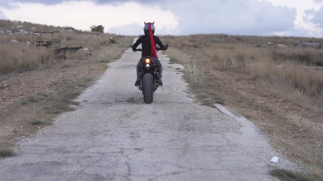 An attractive woman biker in helmet ride away on her motorcycle.
