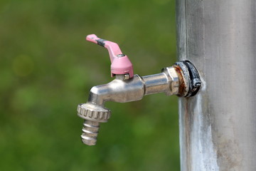 Garden hose tap with dilapidated cracked handle mounted on large metal water tank in local garden...