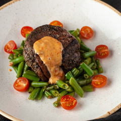 Medium rare mignon fillet roasted with green beans and fresh cherry tomatoes, decorated with creamy sauce for a healthy dinner in a restaurant