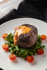 Close up view of a medium rare mignon steak, roasted with green beans and fresh cherry tomatoes, decorated with creamy sauce