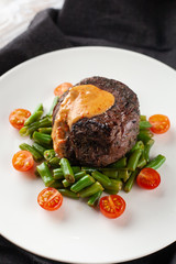 Close up view of a medium rare mignon steak, roasted with green beans and fresh cherry tomatoes, decorated with creamy sauce