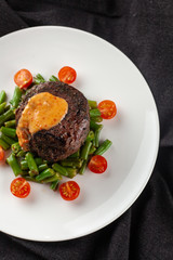 Close up view of a medium rare mignon steak, roasted with green beans and fresh cherry tomatoes, decorated with creamy sauce