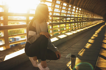 Slender young brunette woman street dancer gymnast sitting and rest with thermo cup on street bridge at sunrise