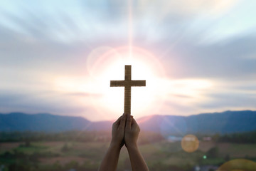 human hands praying to the GOD while holding a crucifix symbol with bright sunbeam on the sky