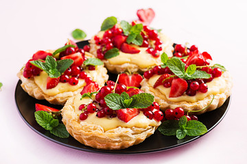 Tarts with strawberries, currant and whipped cream decorated with mint leaves.