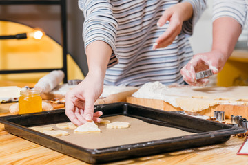 Gingerbread biscuits recipe. Closeup of female hands arranging fir tree shaped dough on sheet pan.
